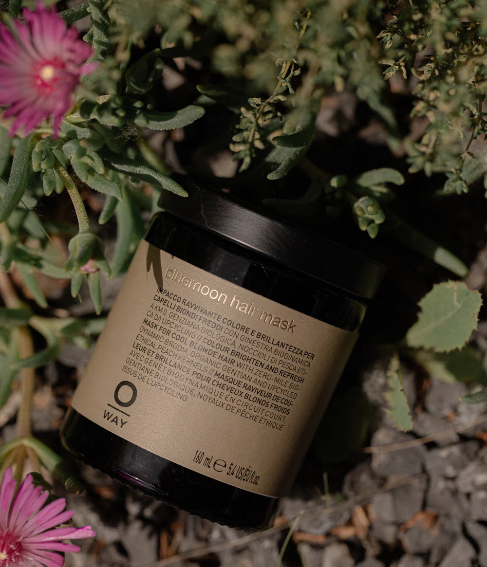 Jar of Oway Midnight Hair Mask surrounded by greenery and pink flowers
