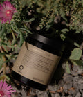 Jar of Oway Midnight Hair Mask surrounded by greenery and pink flowers