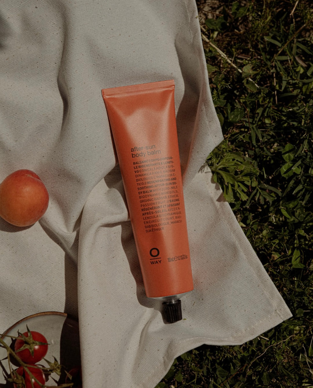 Orange tube of Oway SunWay body lotion held by a person outdoors with greenery in the background