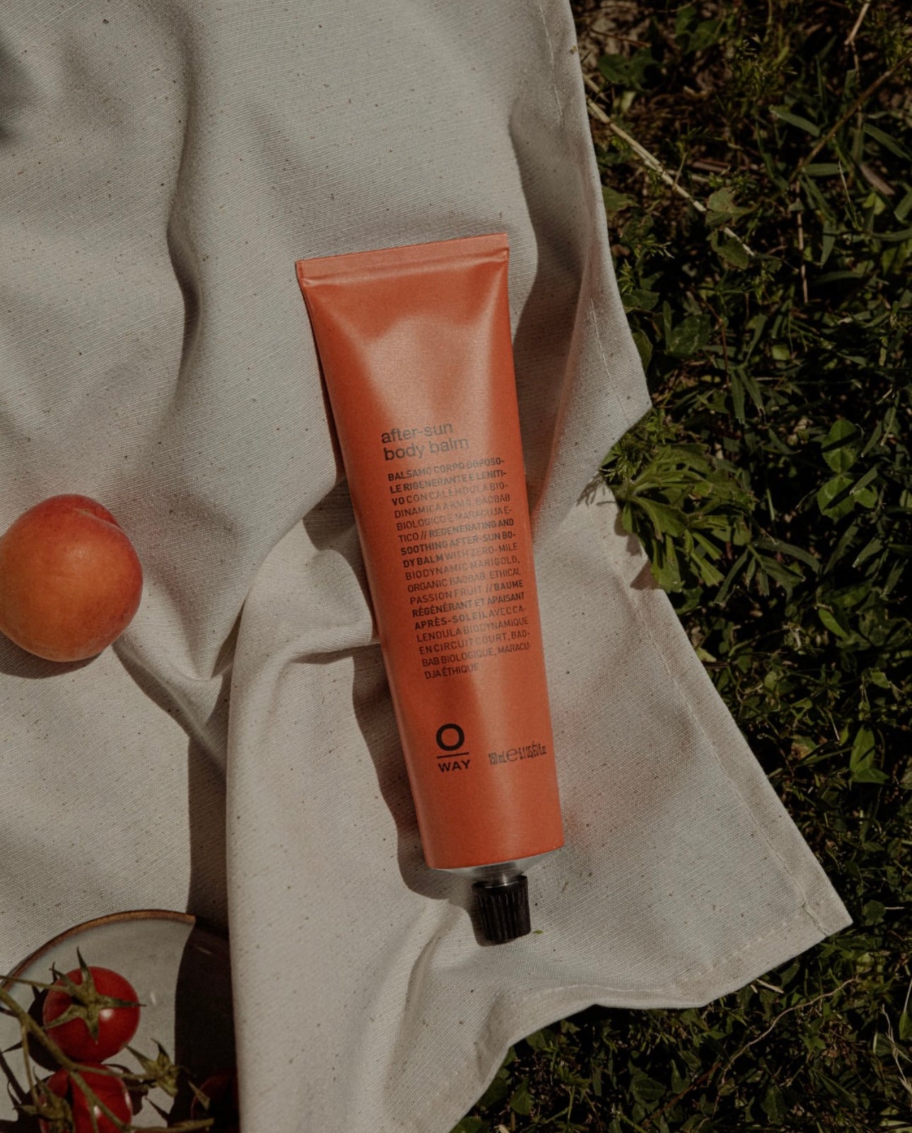 Orange tube of Oway SunWay body lotion held by a person outdoors with greenery in the background