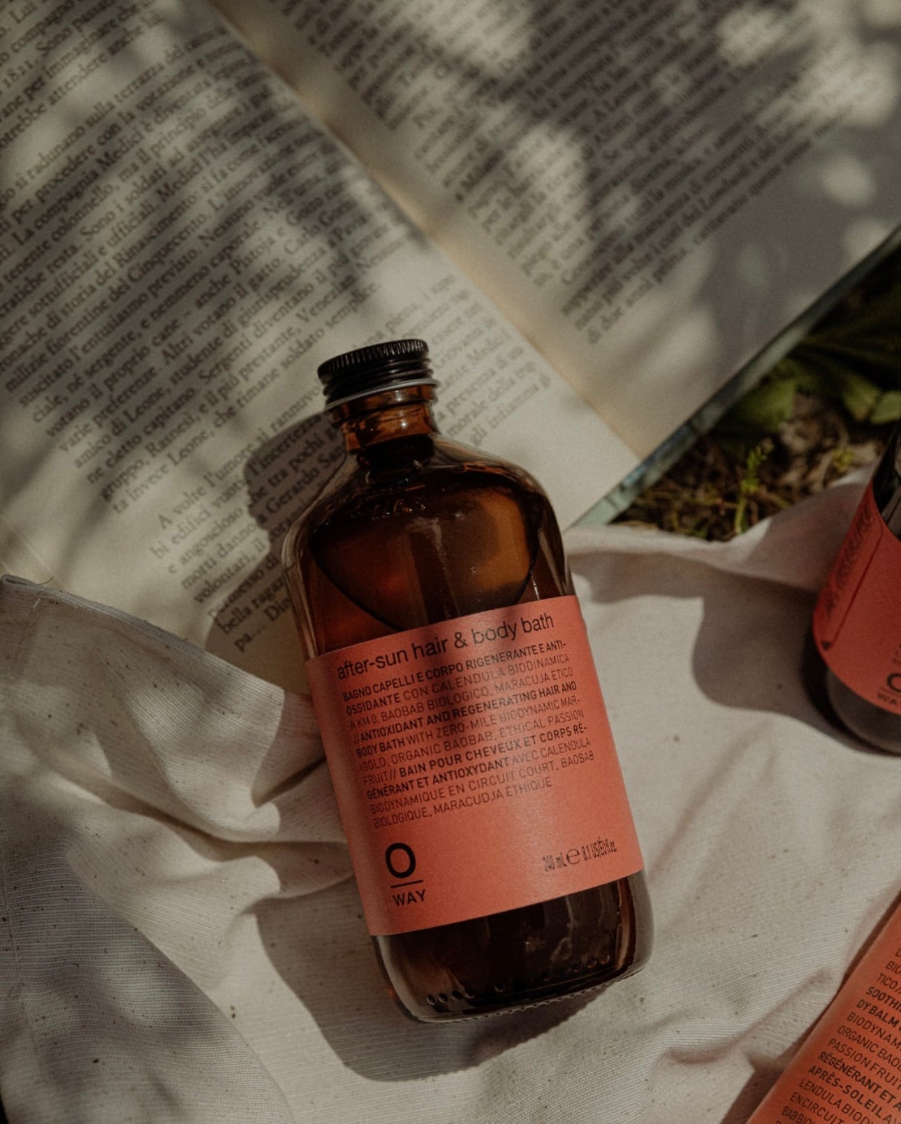 Bottle of Oway after-sun hair and body bath on a textured surface with a book in the background