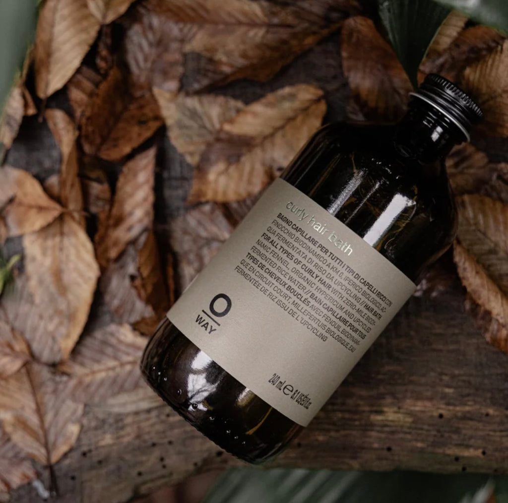 Bottle of Oway curly hair bath on a textured surface with leaves